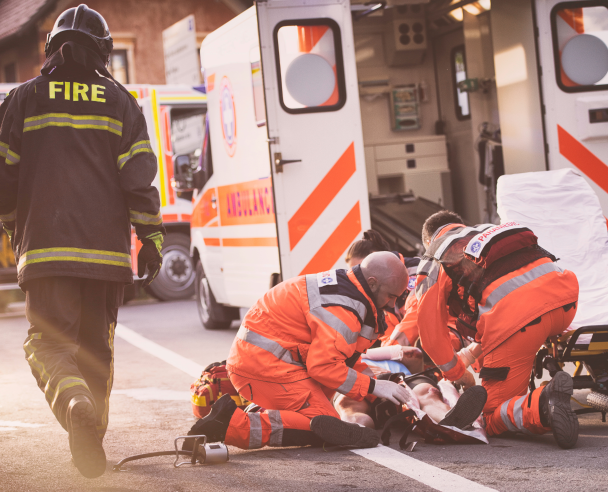 Paramedics in action, performing first aid to a wounded person while a firefighter walks by them