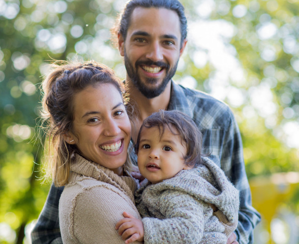 Happy family with a father, a mother and a baby in front of a natural blurred background